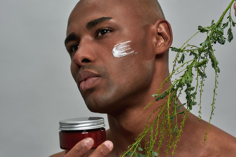 A man using a retinol or AHAs cream on his face while modeling for the camera.