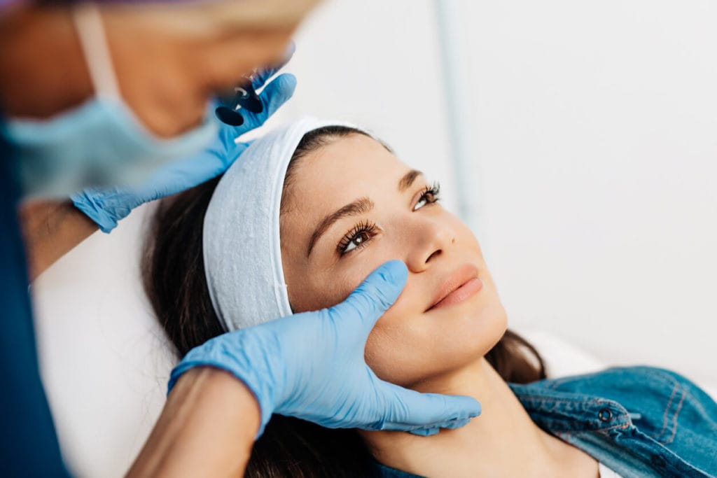 Woman lying down as a dermal filler specialist touches her cheek