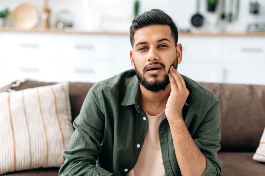 Young male with jaw pain holding side of face experiencing tension