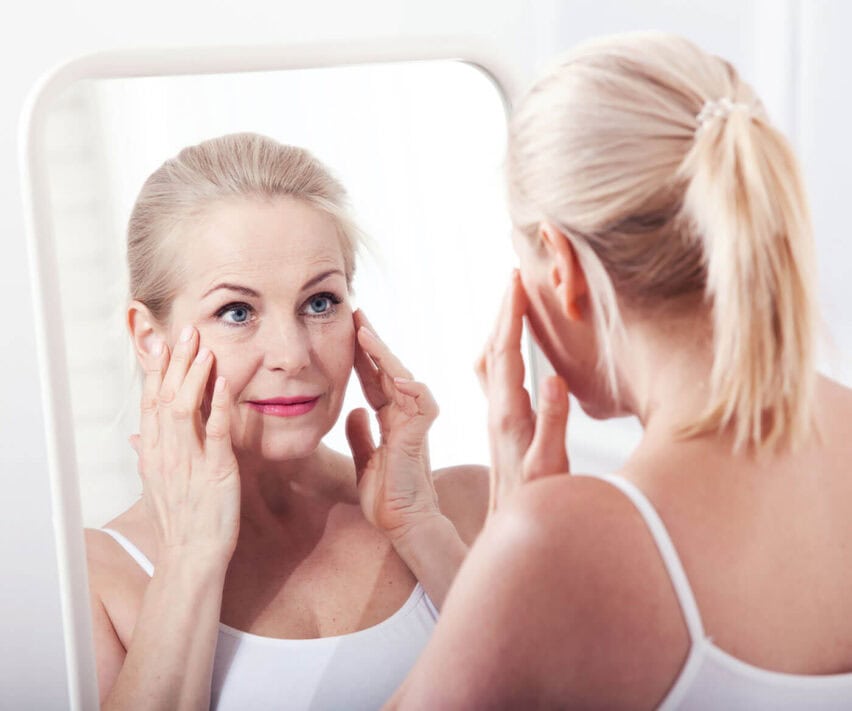 Middle aged woman looking at wrinkles in mirror. Eye wrinkle treatment london