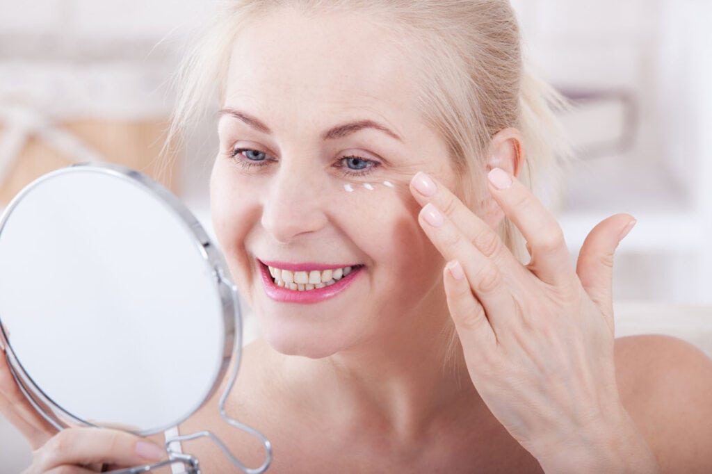 Middle-aged woman smiling at reduced wrinkles in the mirror. Eye wrinkle treatment london, soho